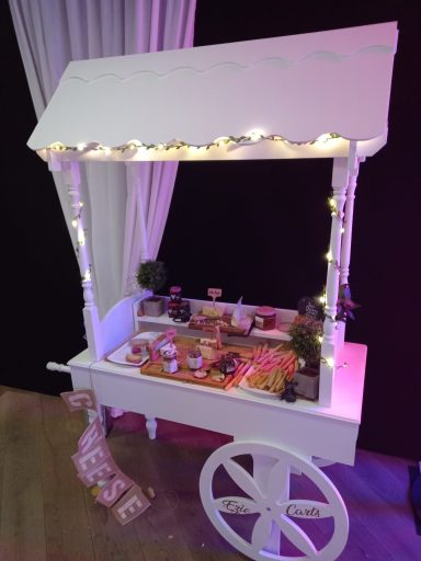 White cart with a canopy, decorated with lights and displaying various treats.