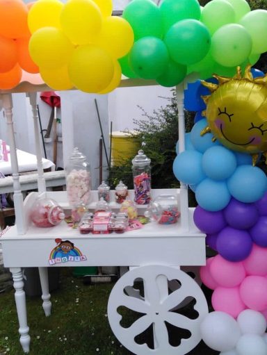 A festive candy cart adorned with colourful balloons and sweets in jars.