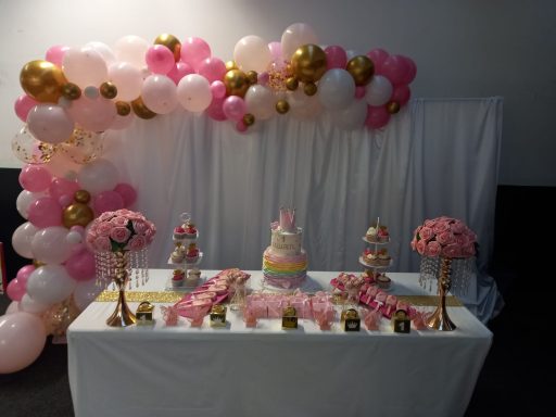 A decorated table with a cake, floral arrangements, and pink and gold balloons.