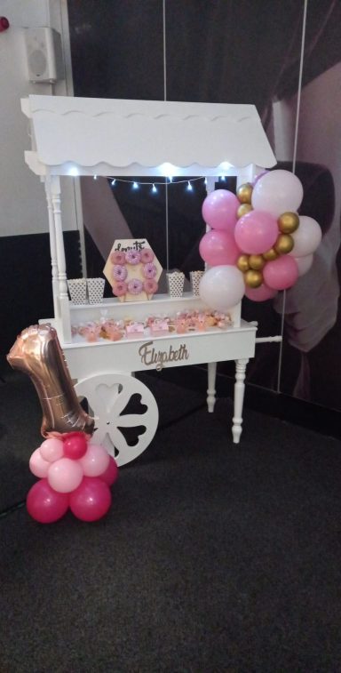 Decorative cart with balloons and sweets, featuring pink and gold colours for a celebration.