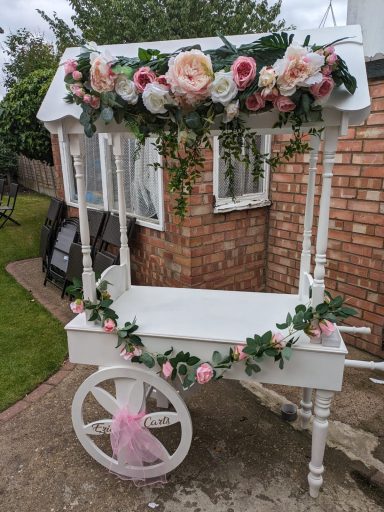 A decorative white cart adorned with pink and white flowers.